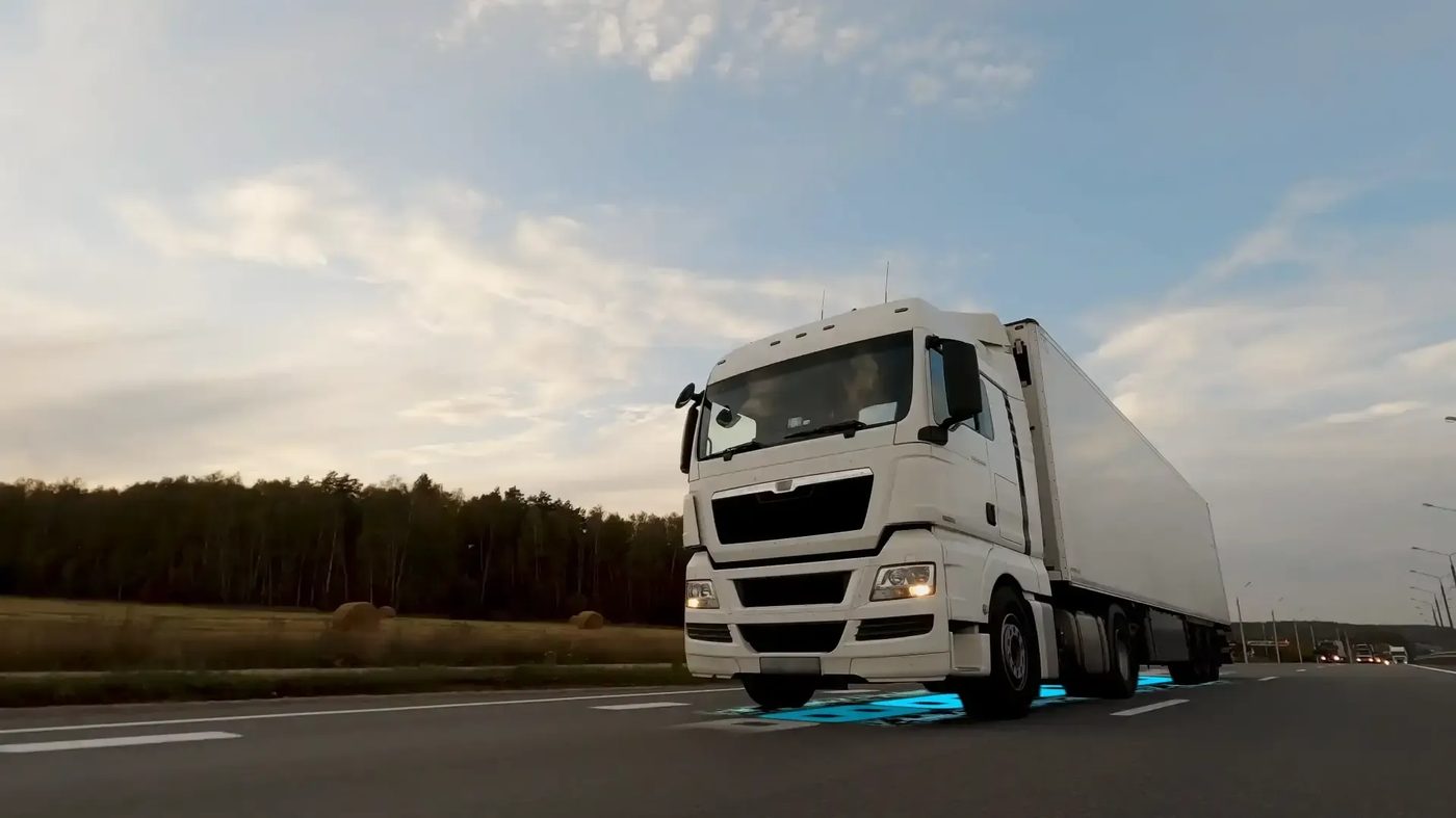 A truck driving over a glowing WibiCharge wireless charging strip on the highway